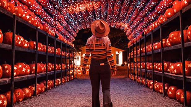A woman in a striped sweater and cowboy hat walks under a jack o'lantern archway at Blaze: Long Island