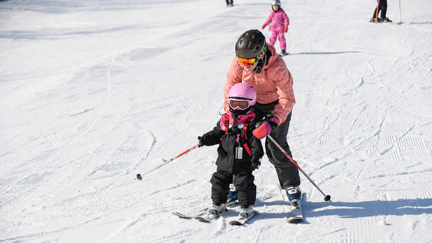 A child in a pink helmet is taught to ski at Greek Peak Mountain Resort
