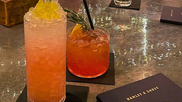 A pink mocktail in a tall glass and a red mocktail in a short glass on black napkins at a bar