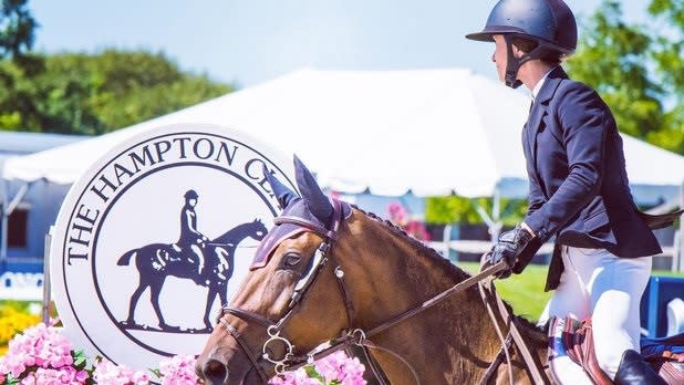 A horse and jockey trots in front of the tent and Hampton Classic sign