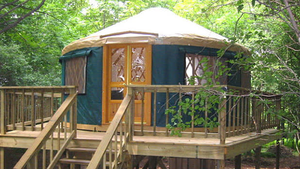 A green and beige canvas yurt set on a wooden platform.