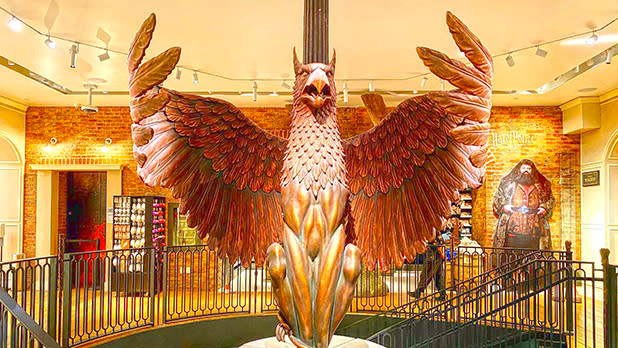 A large gold metal phoenix statue with outstretched wings sitting in the center of a staircase inside the Harry Potter Store