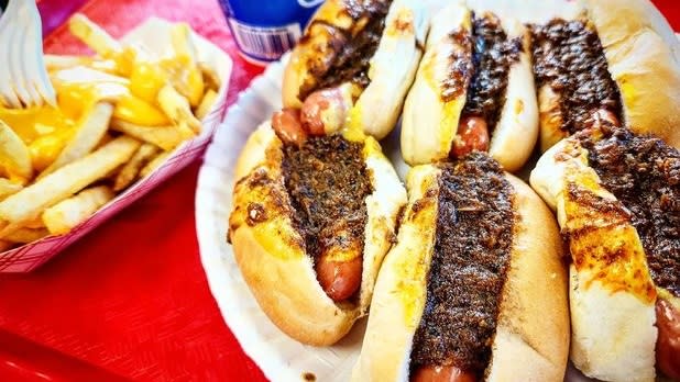 A plate of six "mini dogs" (mini hot dogs) topped with meat sauce sit on a tray with cheese fries