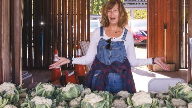 a woman stands with her hands open behind a table filled with cauliflower