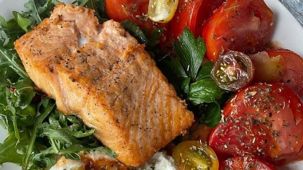 Salmon on a bed of lettuce surrounded by red and yellow cherry tomatoes