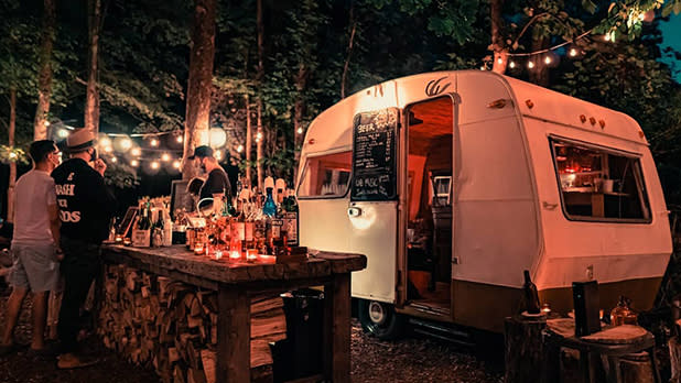 Customers order drinks from a vintage camper that serves as a bar at High Voltage Creek Bar