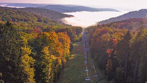 A chair lift cuts through the middle of trees during fall foliage leading into a lake