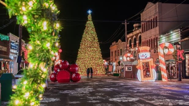 A giant Christmas tree illuminated with bright lights surrounded by giant ornaments, a glowing snowman, candy cane, and other holiday decorations.