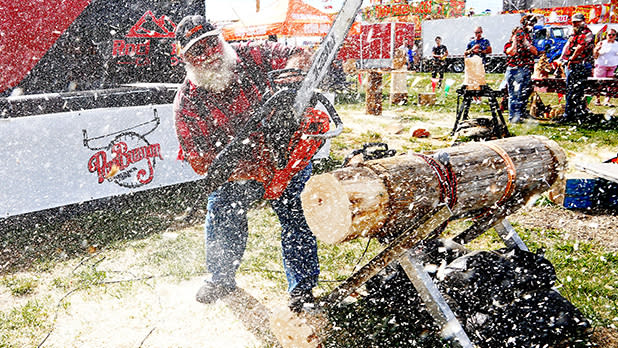 A man with a white beard uses a chainsaw to carve a log on a wooden sawhorse as wood shavings fly through the air at the Paul Bunyan Lumberjack Show during the the Great New York State Fair in Syracuse.