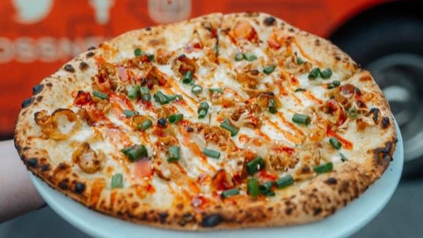 A Chicken Potsticker Pizza by Toss N Fire consisting of chicken potstickers, pecorino, mozzarella, scallions, sesame seeds, and Thai chili sauce.