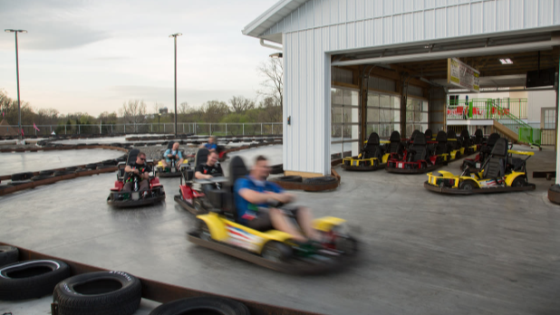 A man in a blue shirt races around a track in a yellow go-kart at The Castle Fun Center