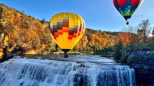 Two colorful hot air balloons float over a waterfall at Letchworth State Park