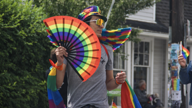A person attends Woodstock Pride wearing a flag, hat, and fan all bearing colors of the Pride Flag