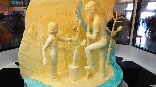 A sculpture made of butter depicting a man and child planting a tree on a fair at the 2024 Great New York State Fair.