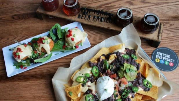 a plate of nachos topped with jalapenos, olives, beans, sour cream, and meat, a flight of beer, and a plate of appetizers