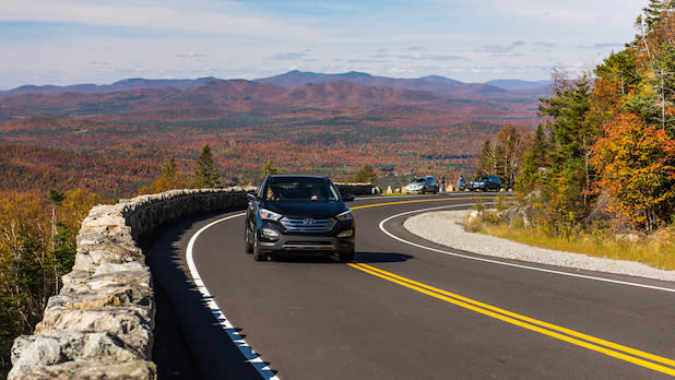 a black car drives up Whiteface Mountain Veterans Memorial Highway with a view of the Adirondack Mountain in fall the background