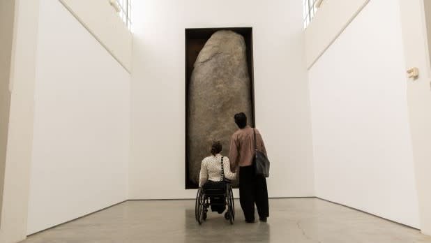 a woman in a wheelchair and a man holding hands while they gaze up at artwork at Dia Beacon