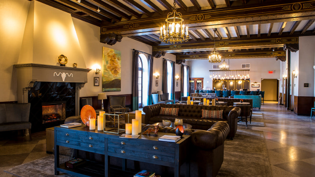 Hotel Saranac's Great Hall Bar replete with a cozy fireplace, leather sofas, decorative candles, and elegant chandeliers. Warm, inviting ambiance with refined decor.