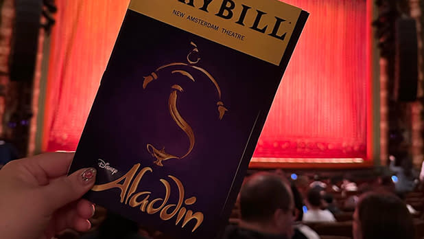 A person holds up a Playbill for the musical Aladdin on Broadway