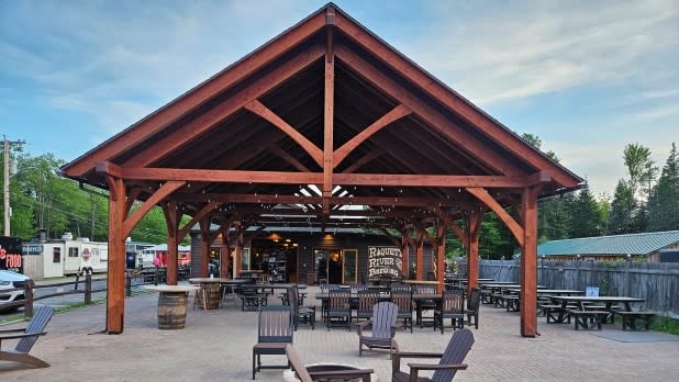 Open-air pavilion outside Raquette River Brewing with wooden beams, Adirondack chairs, and a fire pit in a rustic setting.