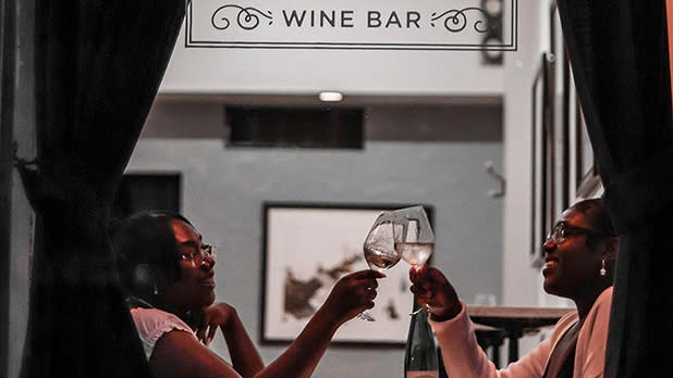 Two women clink glasses at a table inside Apogee Wine Bar in the Finger Lakes