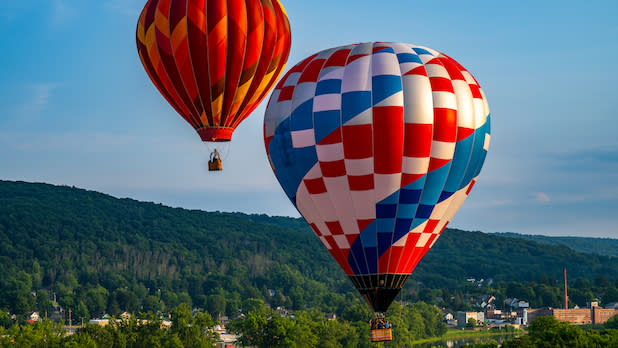 two vibrant hot air balloons float in the sky over rolling hills at the Spiedie Fest & Balloon Rally