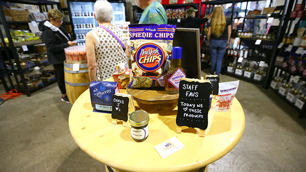 A round wooden display table featuring regional New York State packaged foods, local chips, jams, and small chalkboard signs reading "Staff Favs" at the Great New York State Fair.