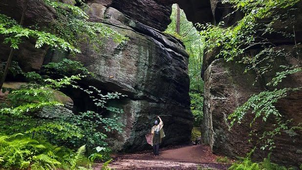 A woman looks up at an archway formed by giant rocks