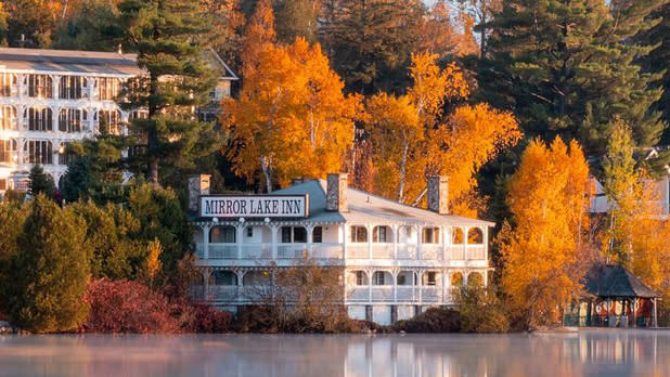 A white Inn sitting next to a lake surrounded by the bright orange leaves of fall