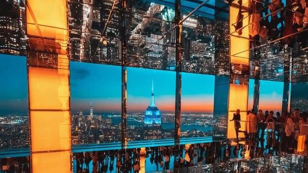 A room with floor to ceiling windows and walls filled with mirrors overlooking the skyline of NYC at sunset