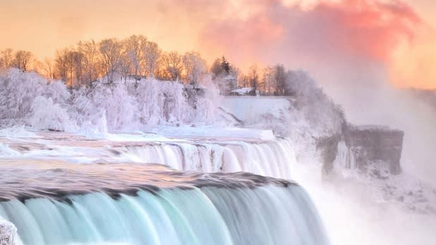 Frosted trees surrounded Niagara Falls with a pink and orange sky in the background during winter