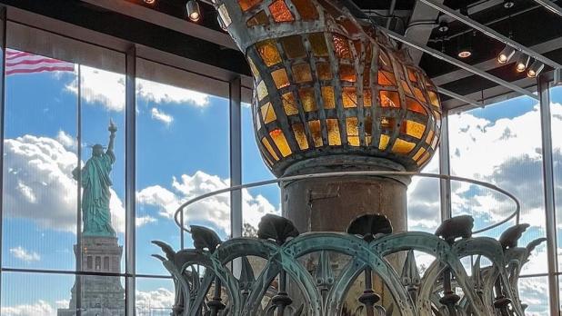 The original torch in the Statue of Liberty Museum with the Statue of Liberty in the background.