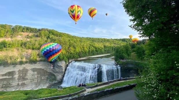 Vibrantly-colored balloons soar over a waterfall at Letchworth on a sunny day