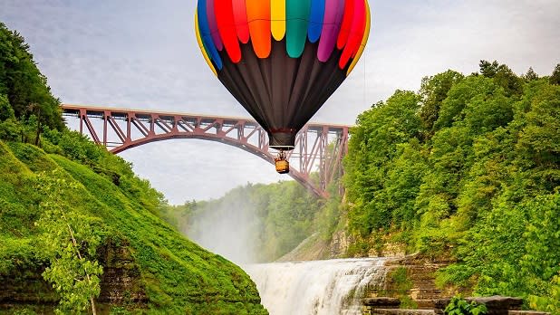 A colorful hot air balloon flies over a waterfall at Letchworth State Park