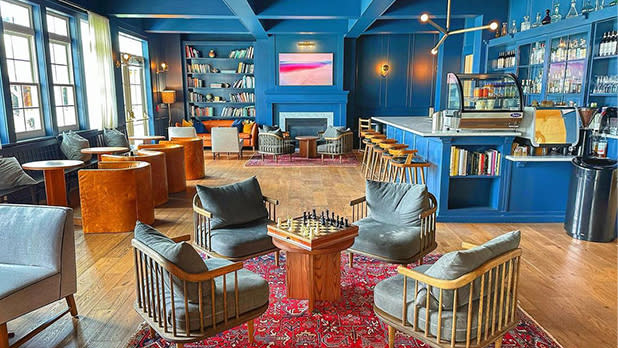 Four wooden chairs with grey cushions sit around a table with a chess table in a bar with a blue interior