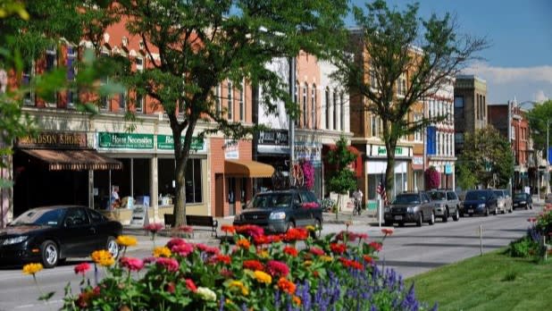 Canandaigua main street with parked cars, storefronts, trees, and colorful flowers in the foreground.