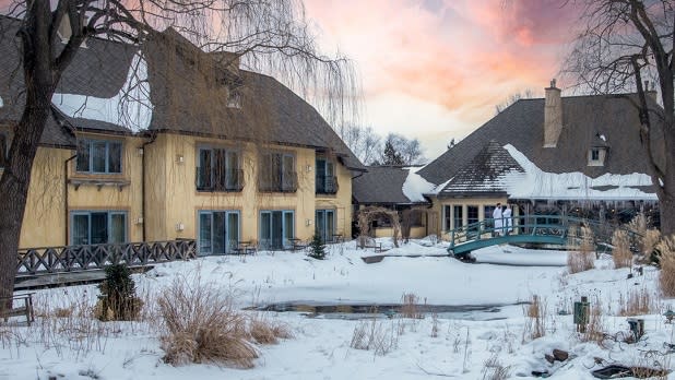 A couple stands on a bridge overlooking the snow-covered Monet-inspired grounds of the Mirbeau Inn and Spa