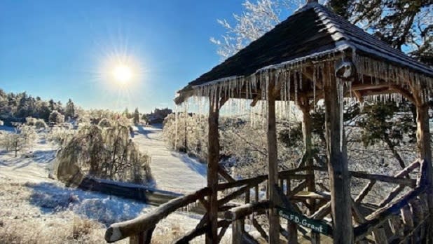 Icicles hang from the roof of a small gazebo surrounded by a snowy landscape