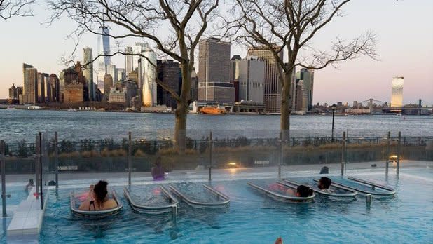 people soaking in an outdoor heated pool looking out at the New York City skyline at dusk