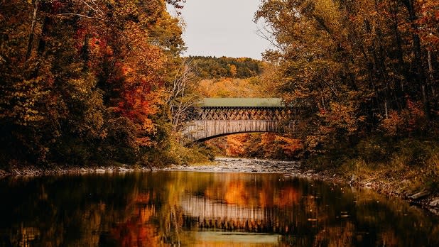 The charming green-roofed Fox Creek Covered Bridge reflected on the water's surface along with stunning scenery of fall foliage
