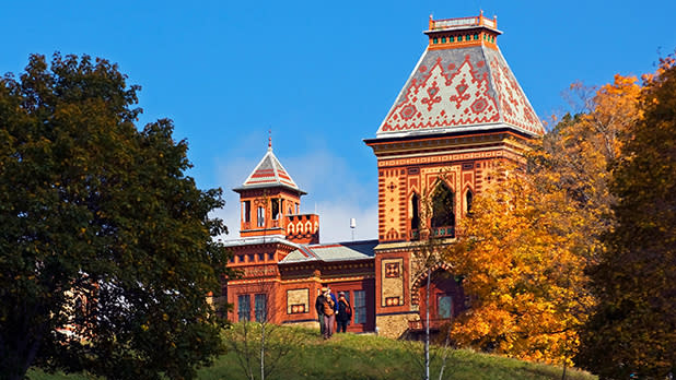 The sun shining on Olana State Historic Site with yellow trees to the right and green trees to the left