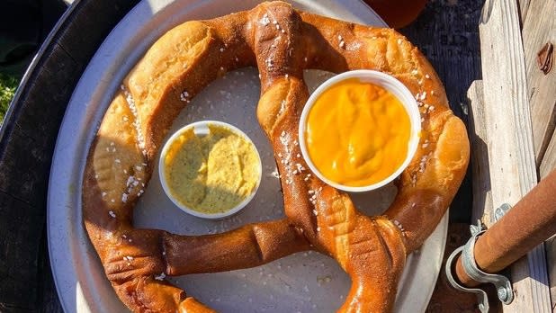 A large salted soft pretzel with cups of cheese and spicy mustard