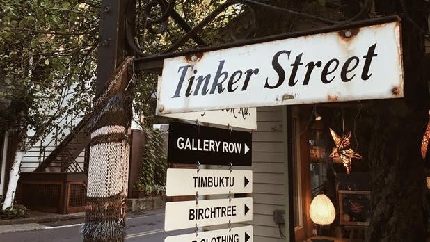 A white sign that says "Tinker Street" in black font with a list of shop names underneath
