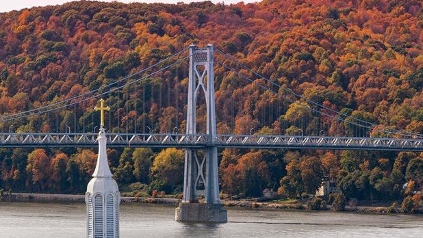 Fall foliage decorates the mountains behind a grey bridge