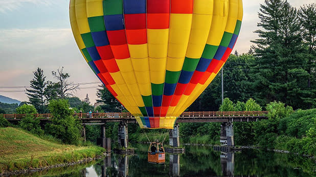 A colorful hot air balloon soars over a waterway at the Great Wellsville Balloon Rally