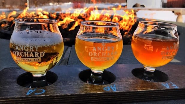 Three Angry Orchard tasting glasses lined up in front of a fire pit