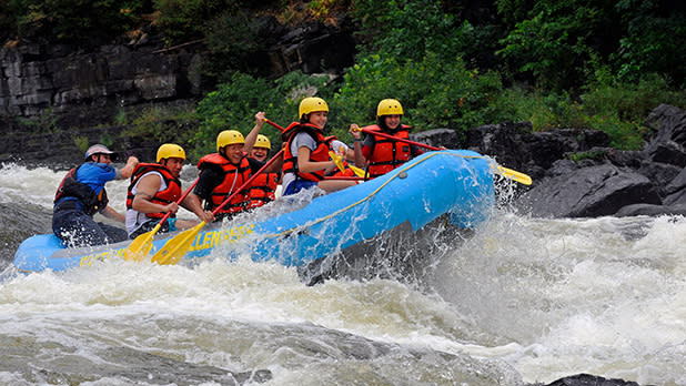 A group of people in yellow safety hats and red life jackets whitewater rafting along a river