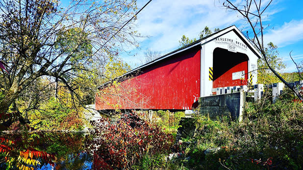 The Rexleigh Bridge, with its striking red facade and white trim portal stands over Battenkill River amid colorful foliage
