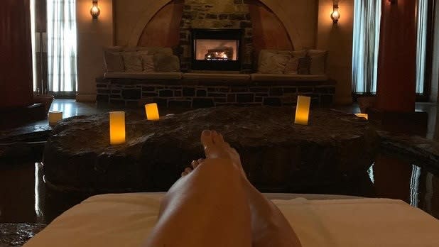 person lounging in front of a fireplace surrounded by candlelight