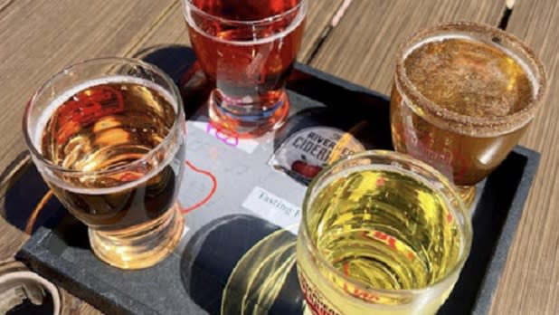 Four glass of cider ranging from dark to light on a black flight tray